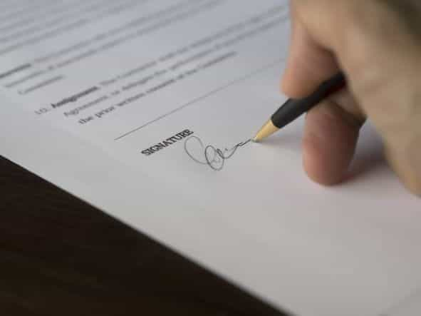 A hand signing a document with a pen.