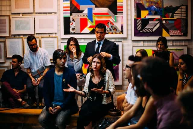 A group of people speak in a gathering with colorful art behind them.